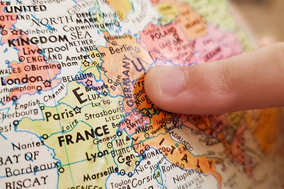 Finger pointing at Germany on a colourful map of Europe, surrounded by neighbouring countries.