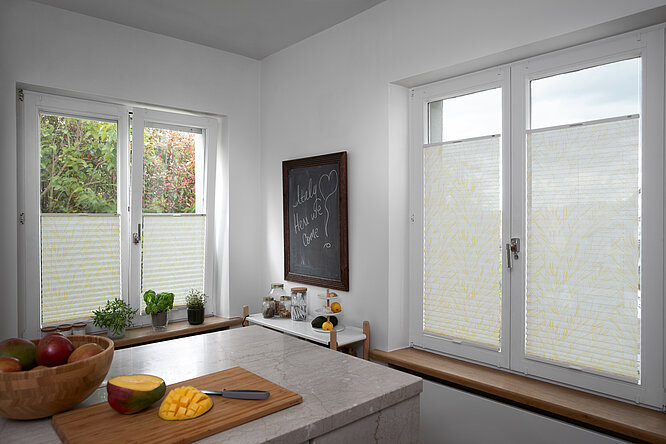 Küche mit halbtransparenten Plissees im gelben Gräserdesign an den Fenstern.