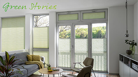 Wohnzimmer mit grünen Wabenplissees an den Fenstern und dem Schriftzug „Green Stories“ oben links.
