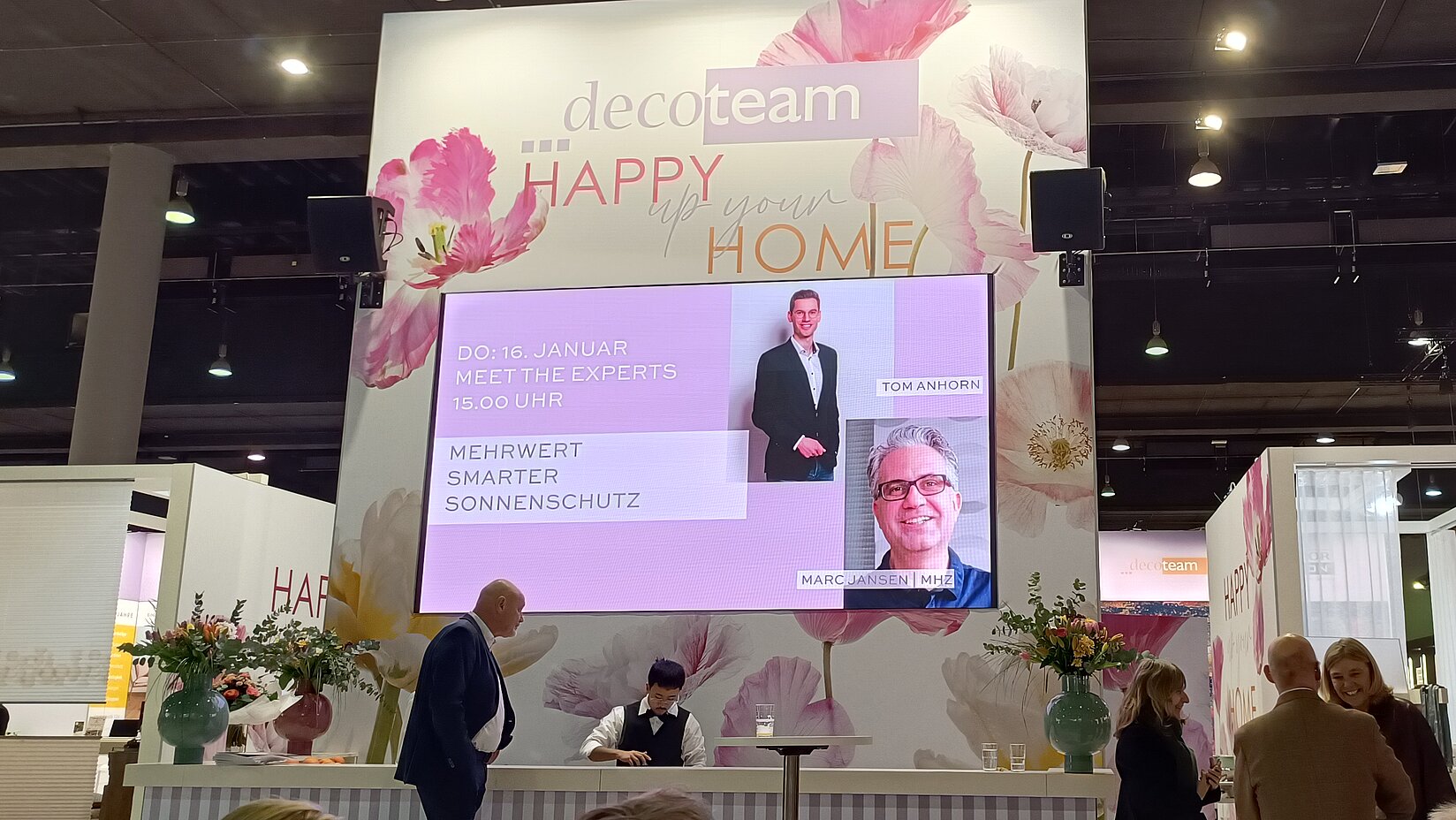 Große Messebühne mit Bildschirmankündigung „Meet the Experts“ zum Thema smarter Sonnenschutz, umgeben von Messebesuchern.