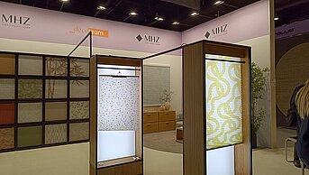 MHZ Messestand mit beleuchteten Plissee-Displays und Musterwand zur Präsentation moderner Sicht- und Sonnenschutzsysteme.