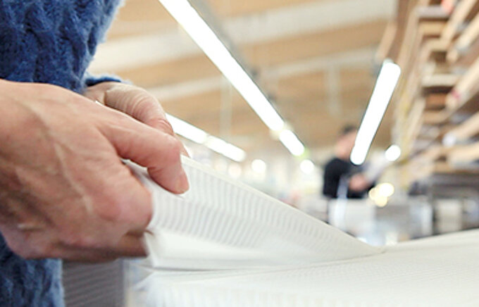 Nahaufnahme von Händen bei der Herstellung eines Plissees in einer Produktionshalle.