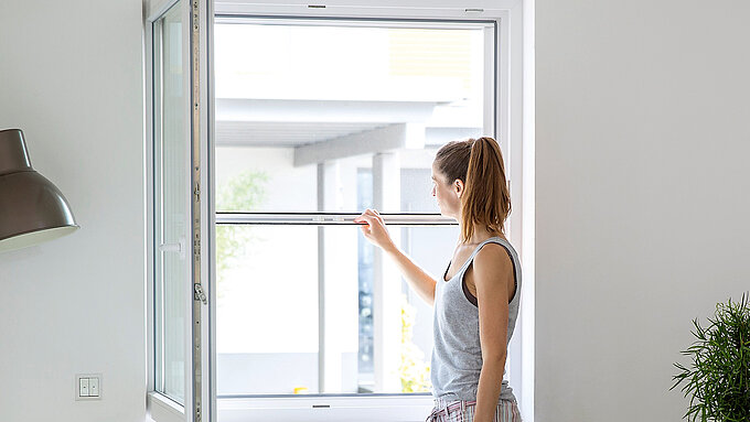 Woman uses manual insect screen roller blind on an open window.