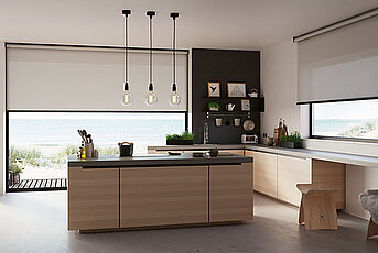 Moderne Küche mit großer Kochinsel und zwei Fenstern mit hellen Rollos, Blick auf Dünenlandschaft am Meer.