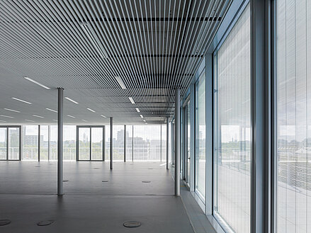 Innenraum eines modernen Büros mit Metallbehang Senn an raumhohen Glasfassaden und strukturierter Decke.