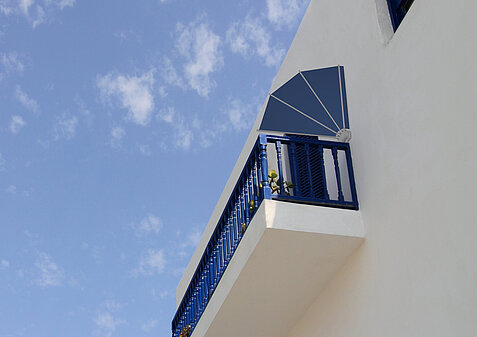 Balkon mit blauer Metallbrüstung und seitlich montierter fächerförmiger Markise an weißer Fassade