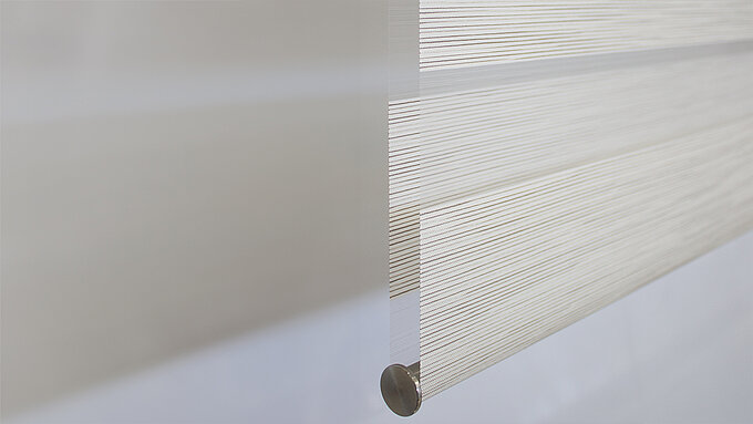 Nahaufnahme der Stoffkante eines weißen MHZ Doppelrollos mit feiner horizontaler Streifenstruktur und metallischem Abschlussprofil.