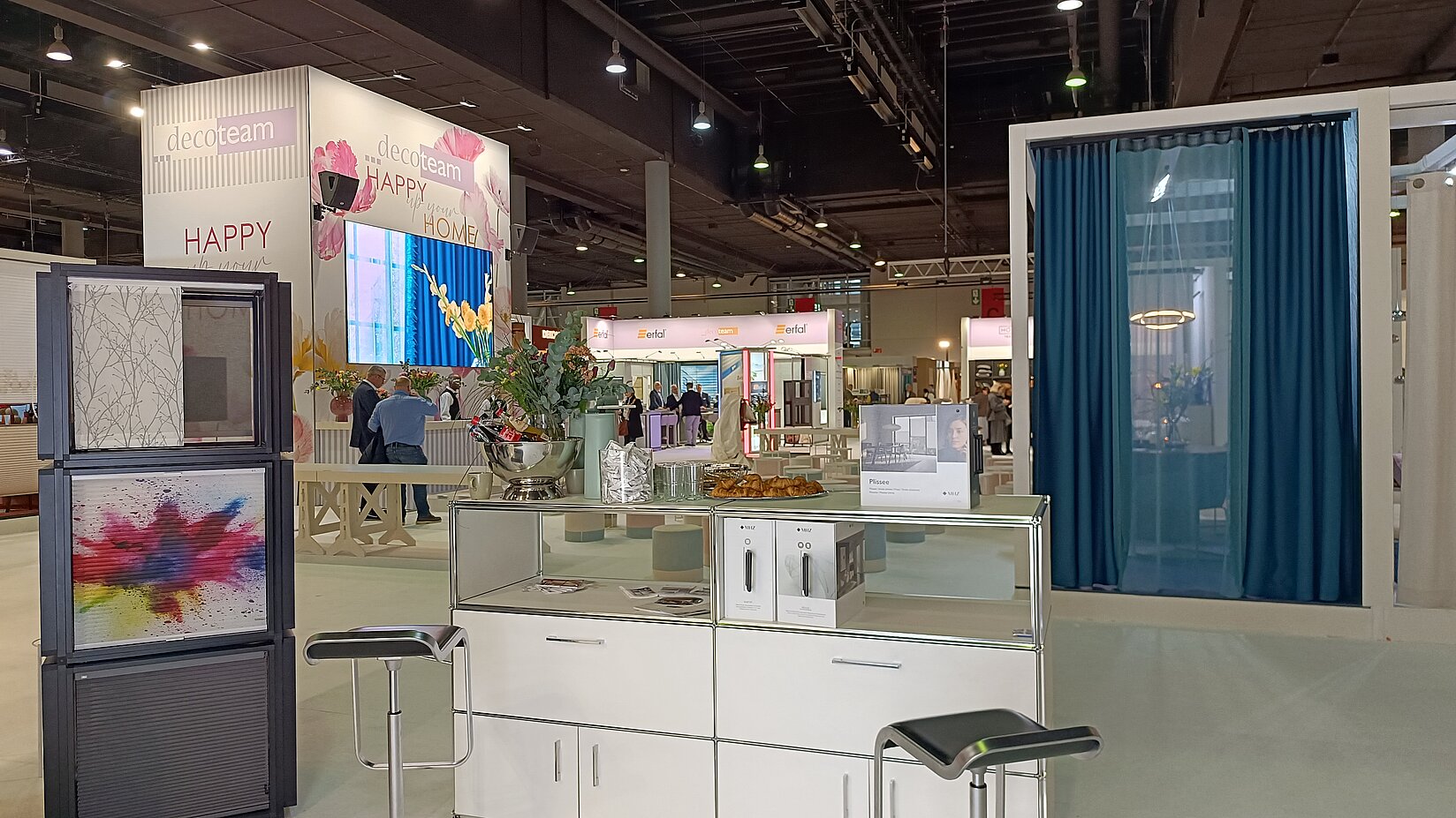 Messestand mit ausgestellten Plissee-Mustern und einem Fensterdisplay mit blauem Vorhang als Sicht- und Sonnenschutz.