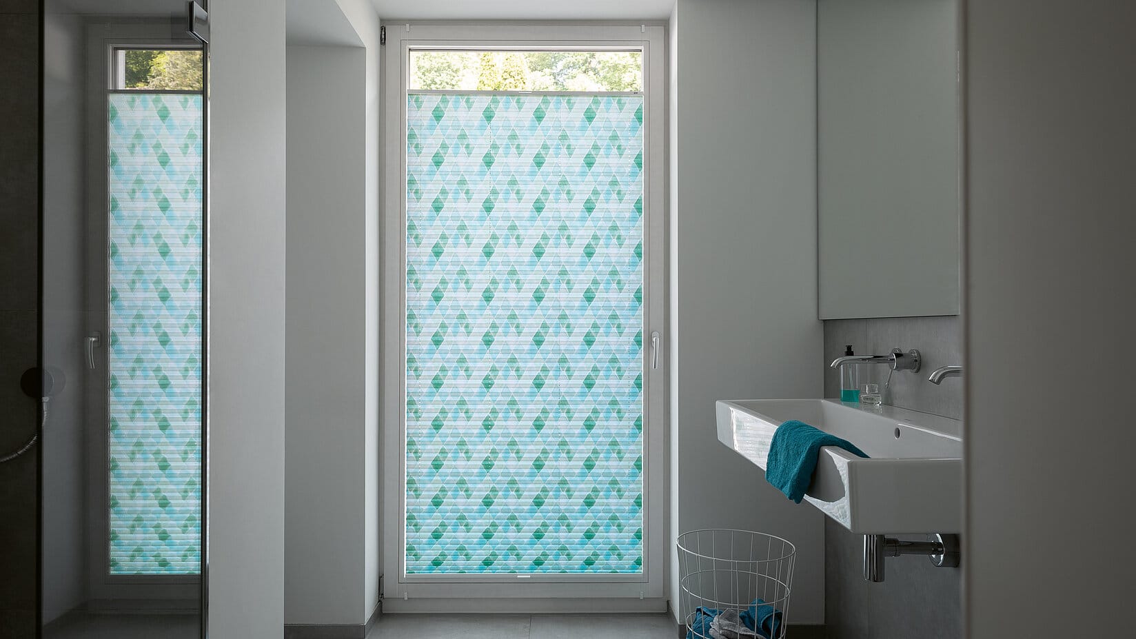 Badezimmer mit bodentiefem Fenster und einem Plissee in Aquarelloptik in verschiedenen Blautönen.
