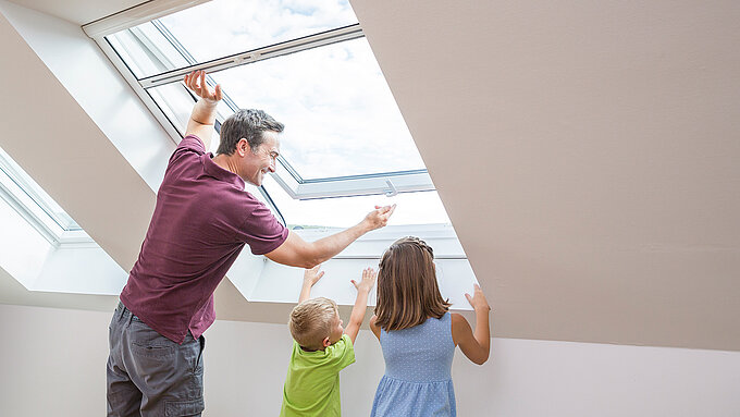Father with two children opens roof window with insect screen roller blind in attic.