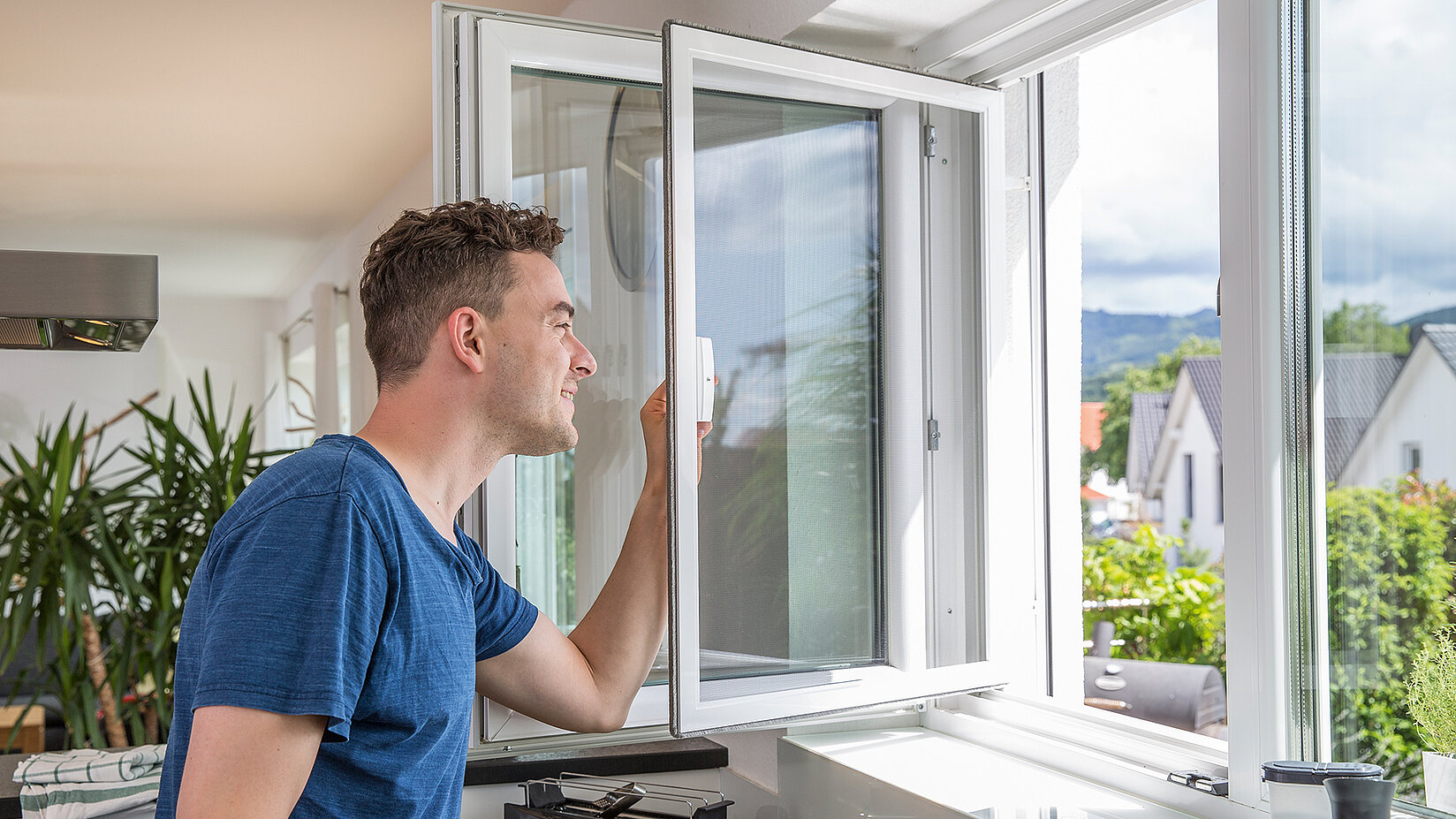 Man opens a pivoting window with insect screen in a bright room.