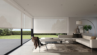 Lichtdurchlässige Rollos an bodentiefen Fenstern in einem hell eingerichteten, modernen Wohnzimmer mit weißen Möbeln und Naturakzenten.