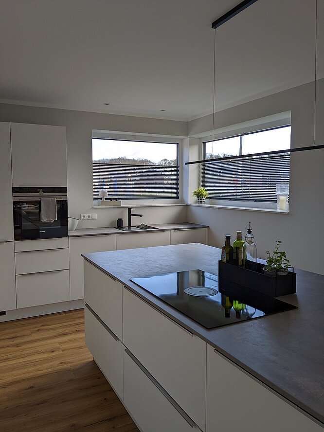 Moderne und minimalistische Küche mit Kücheninsel und frei verschiebbarer Jalousie in schwarz am Fenster.