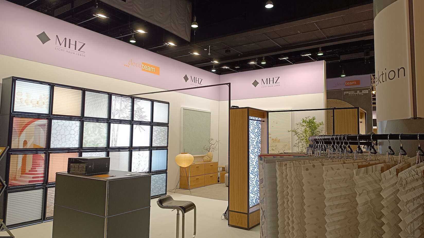 MHZ Messestand mit Musterwand und aufgehängten Plissee-Stoffmustern zur Präsentation von Sicht- und Sonnenschutzlösungen.