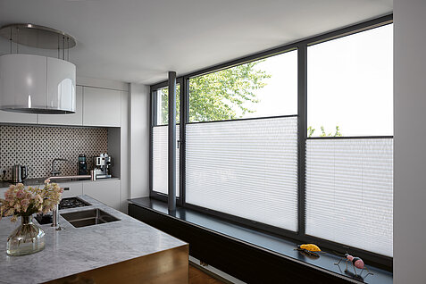 Weiße Plissees im unteren Fensterbereich in moderner Küche mit großen Fensterflächen.