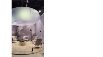 Stimmungsvoll beleuchteter Loungebereich mit Sesseln und rundem Teppich unter einem schwebenden textilen Objekt auf der imm cologne.